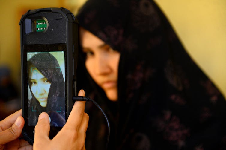 Un teléfono celular que muestra el rostro de una mujer se sostiene cerca del rostro de la misma mujer.