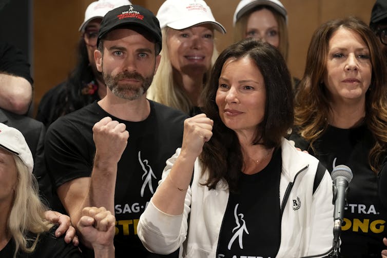 A woman crowd of people wearing SAG-AFTRA shirts hold their fists up