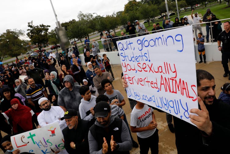 A group of protesters standing outside a library; one carries a sign that says 'Quit grooming students, you sexually perverted animals'