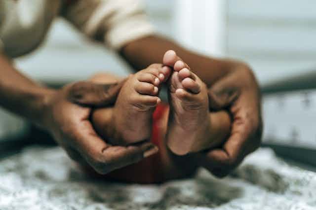 Une paire de mains entoure les pieds d'un bébé au niveau de la cheville.