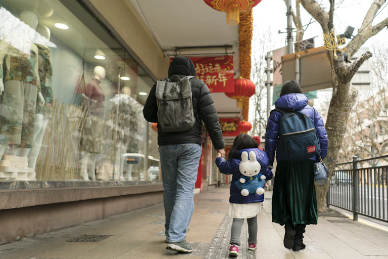 A girl and two adults walk away from the camera by a shop with mannequins in the window.