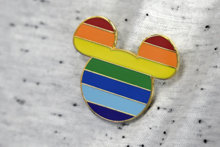 a mickey mouse pin with rainbow colors adorns a worker's shirt
