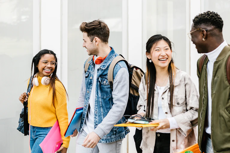 Holding books and carrying backpacks, a group of multiracial students chat on the way to class.