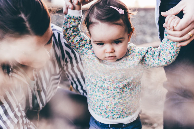 two adults help small child walk by holding her hands