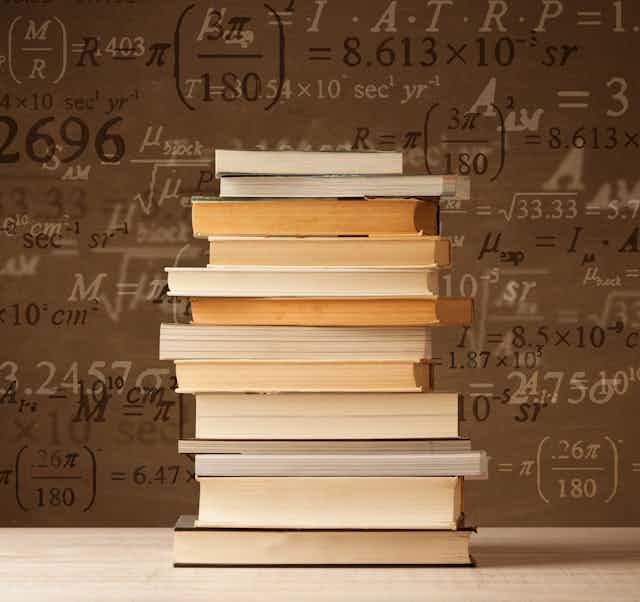 A stack of books sits on a table with math formulas in the background.