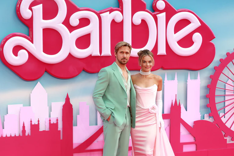 Man and woman pose for photographers in front of a billboard promoting a film