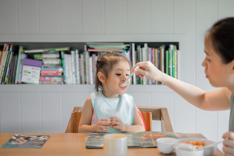 parent feeds child by spoon at table