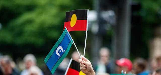 A crowd of people waving small hand-held Aboriginal and Torres Strait Islander flags.