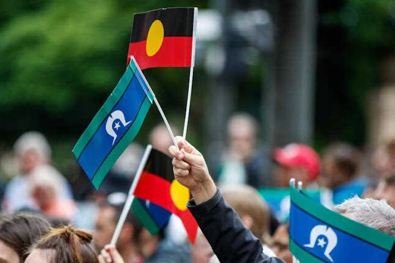 A crowd of people waving small hand-held Aboriginal and Torres Strait Islander flags.