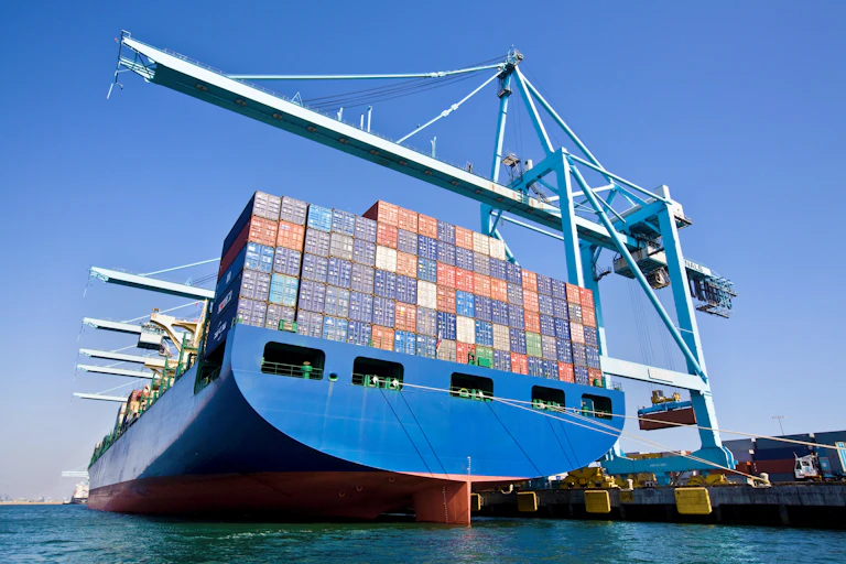 A large container ship in port, seen from the back.