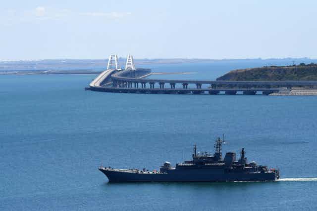 A view of the Kerch bridge with a Russian navy ship in front of it.