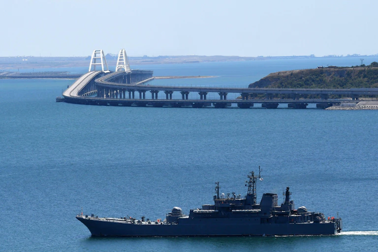 A view of the Kerch bridge with a Russian navy ship in front of it.