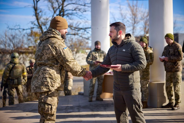 Ukrainian president Volodymyr Zelensky shaking hands with a soldier in fatigues.