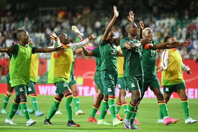 A group of African women in football gear gesture with their arms, a sense of victory with smiles on their faces.