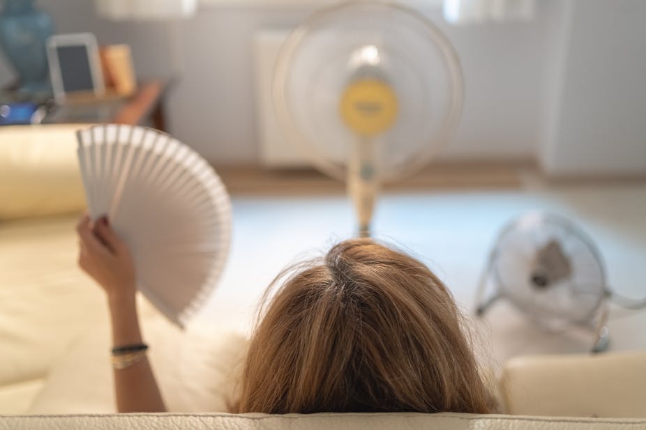 Woman sitting on a sofa with several fans giving her air.