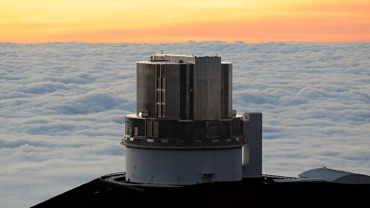 A cylindrical building sitting on a cliff overlooking a sunset.