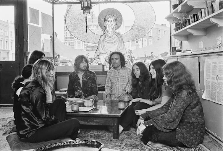 A group of young men and women seated on the floor around a table that has objects on it.