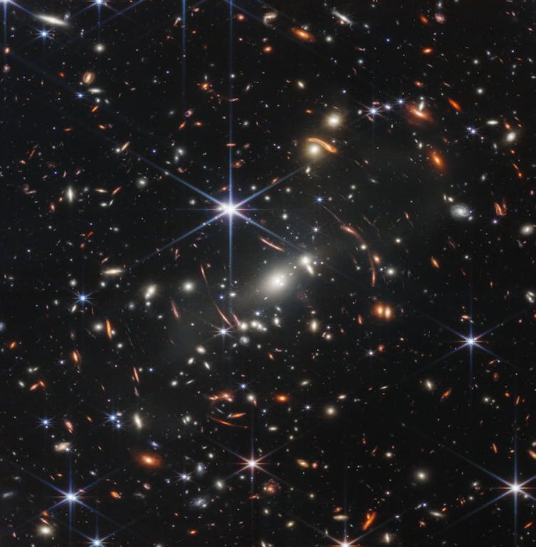Image of lightly colored galaxies and stars against dark background