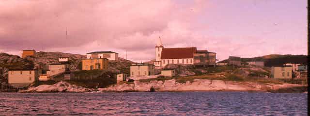 An old photo of  a sea side town with a few buildings and a church in the centre.