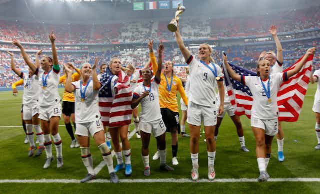 US soccer players draped in national flags celebrate, one holds aloft a trophy.
