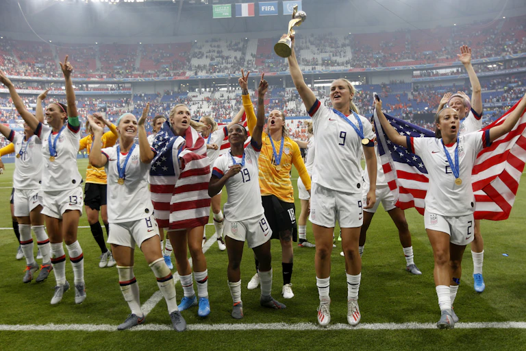 US soccer players draped in national flags celebrate, one holds aloft a trophy.