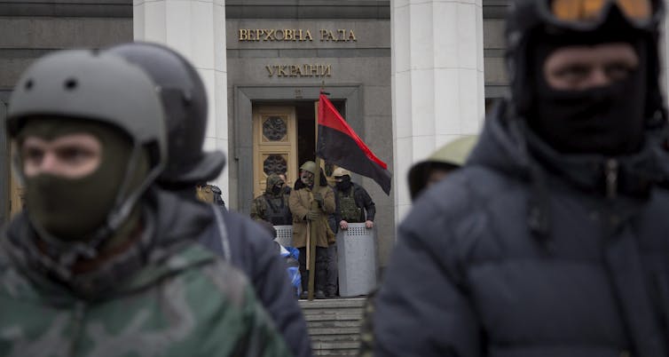 Men in helmets and battle fatigues stand in front of a government building.