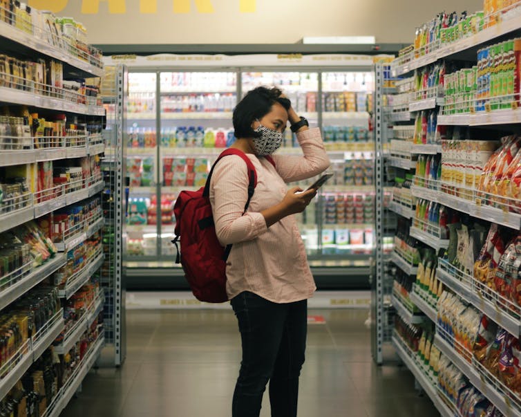 Woman in a mask grocery shops, with a list on her phone