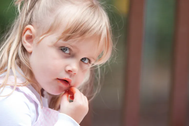 A young blond child finishes what's left of a Cheeto.