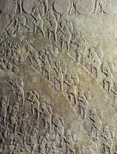 A relief shows rows of men lugging heavy items as they plod up a hill.