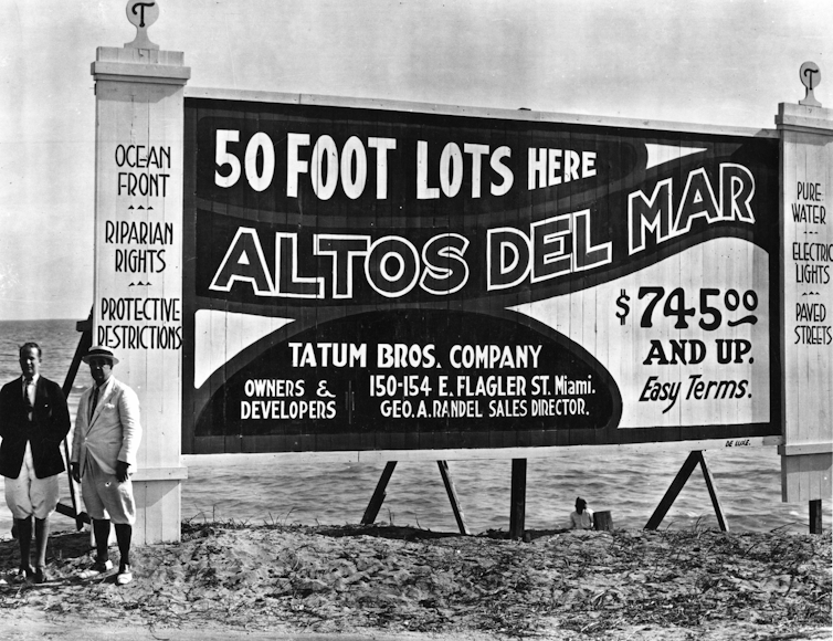 Two men stand next to a large billboard reading: 50 foot lots at altos Del Mar. $745 and up.