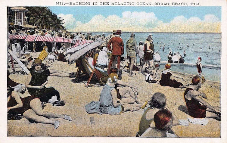 Women in 1920s-style bathing suits lounge on a beach in Florida.