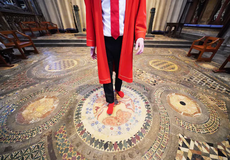 A man in red socks stands on an ancient decorative mosaic floor in Westminster Abbey.