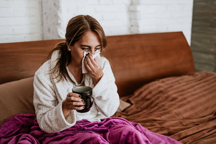 A woman in pyjamas blowing her nose.