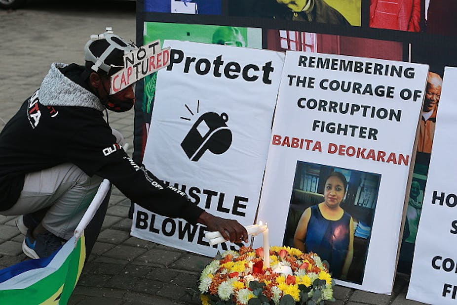 A man lights a candle in front of a poster saying 'Protect Whistleblowers' and another with the image of a woman, Babita Deokaran, a murdered whistleblower. 