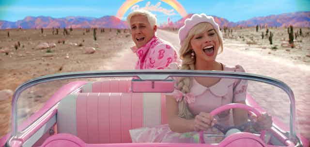 Ryan Gosling as Ken and Margot Robbie as Barbie both wear pink and drive down a desert road. 