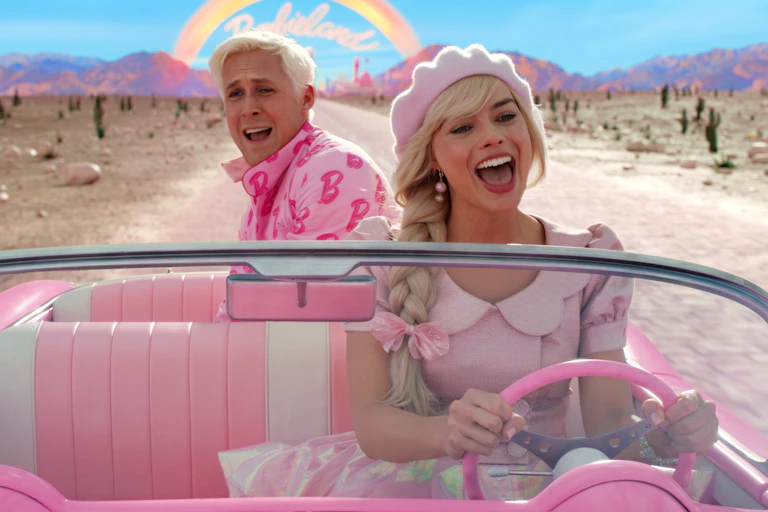 Ryan Gosling as Ken and Margot Robbie as Barbie both wear pink and drive down a desert road.