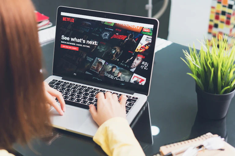 Woman typing on laptop, screen shows Netflix log in page that says "See what's next"