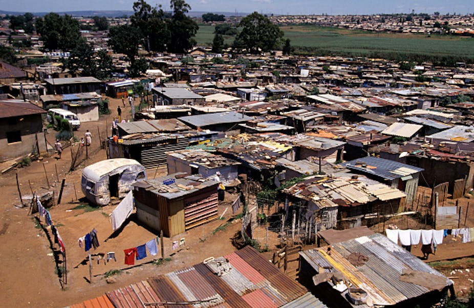 Aerial view of crowded settlement of small structures, with unpaved spaces between them 