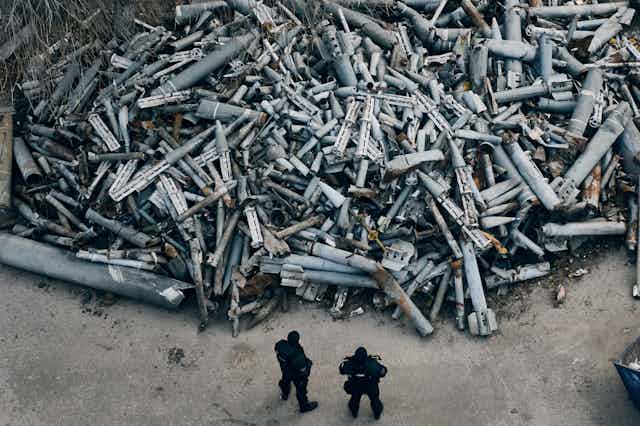 Two police officers stand looking at a huge pile of weapons debris.