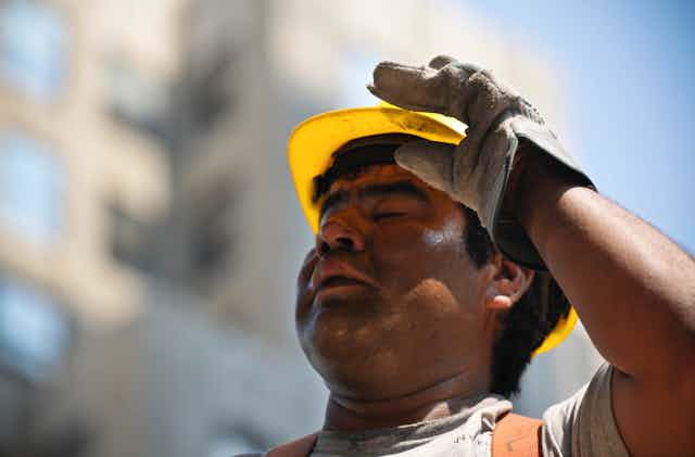 A sweating construction worker adjusts his hard hat.