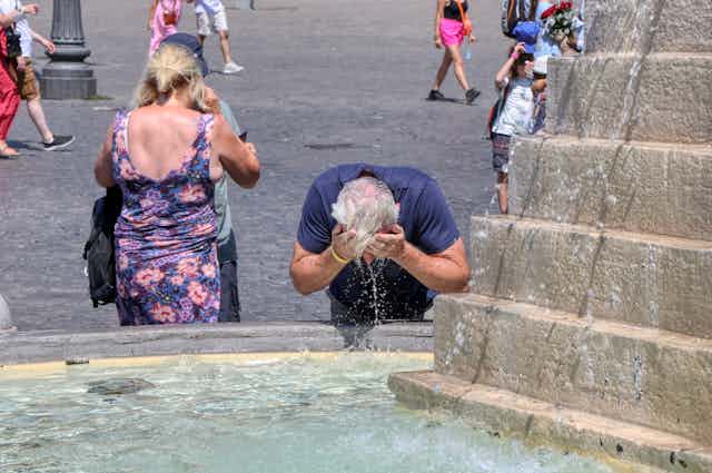 Un turista se refresca la cabeza con agua de una fuente en un día de mucho calor.