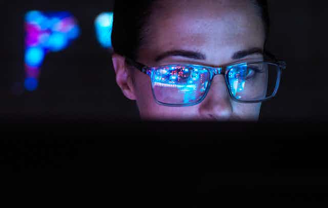 A woman wearing glasses that reflect a computer screen.