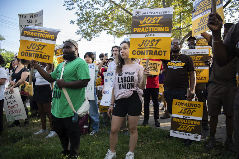 A group of people hold aloft placards stating 'UPS Teamstrers, Just Practicing for a Just Contract.'