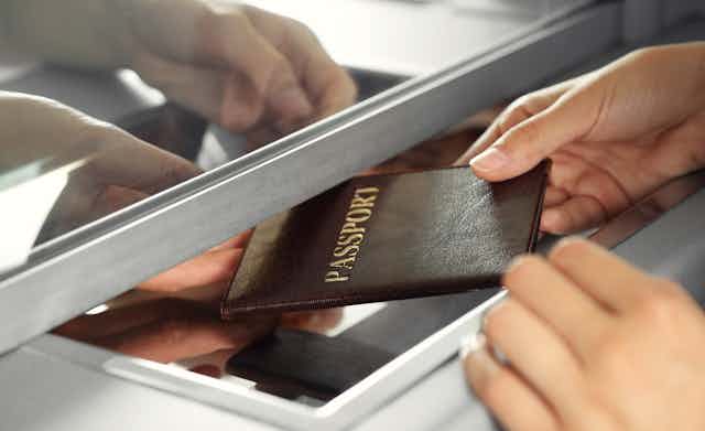 Hands passing a passport to another person through a window