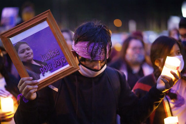 A man holds a candle and a photo of a woman that reads: Justice pour Joyce