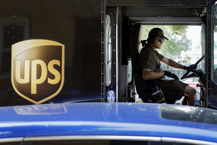 A uniformed employee sits in the driver's seat of a truck with UPS written on the side.