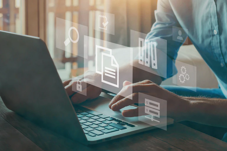 A photo of a man working on a laptop. Graphic symbols of files and documents are above the laptop.