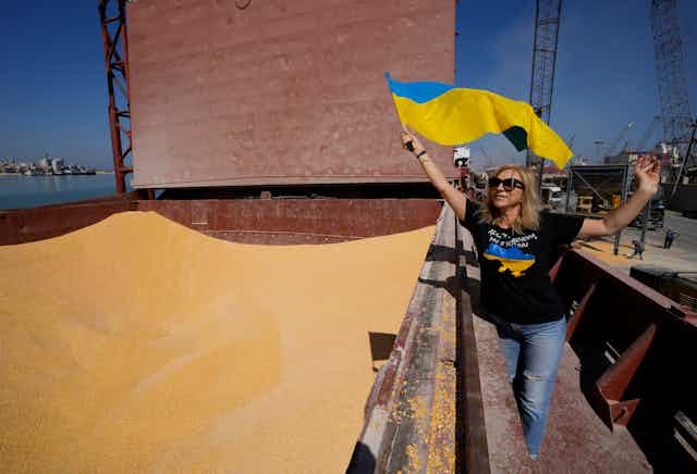 a woman waving ukrainian flag walks near a container full of corn
