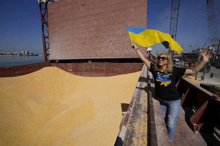 a woman waving ukrainian flag walks near a container full of corn