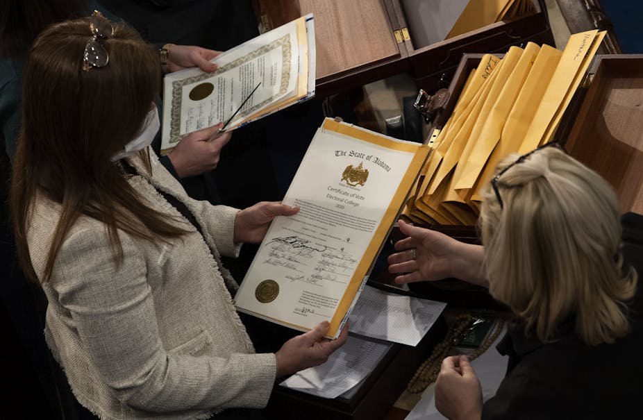 Two women hold documents with seals for the state of Alabama with the wording, “Certificate of Vote, Electoral College, 2020.”